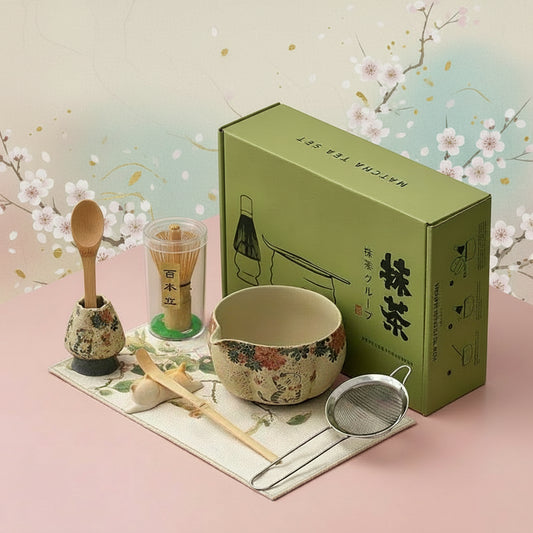 Tea-making set with a green box, bowl, spoon, and strainer on a pink surface with cats in the background.