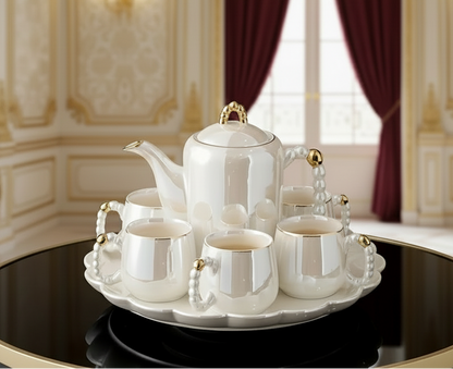 White ceramic tea set with gold accents on a tray, placed on a reflective surface.