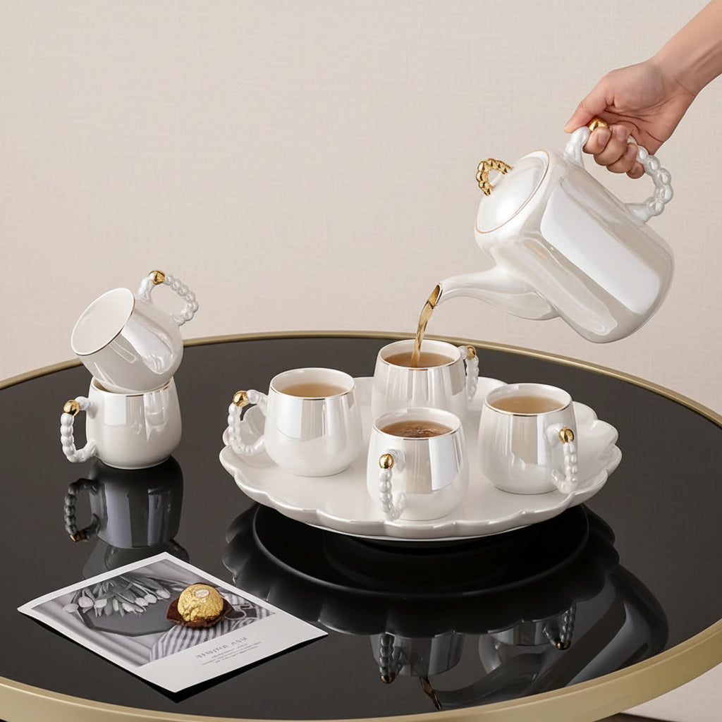 White ceramic tea set with a person pouring tea into a cup on a reflective surface.