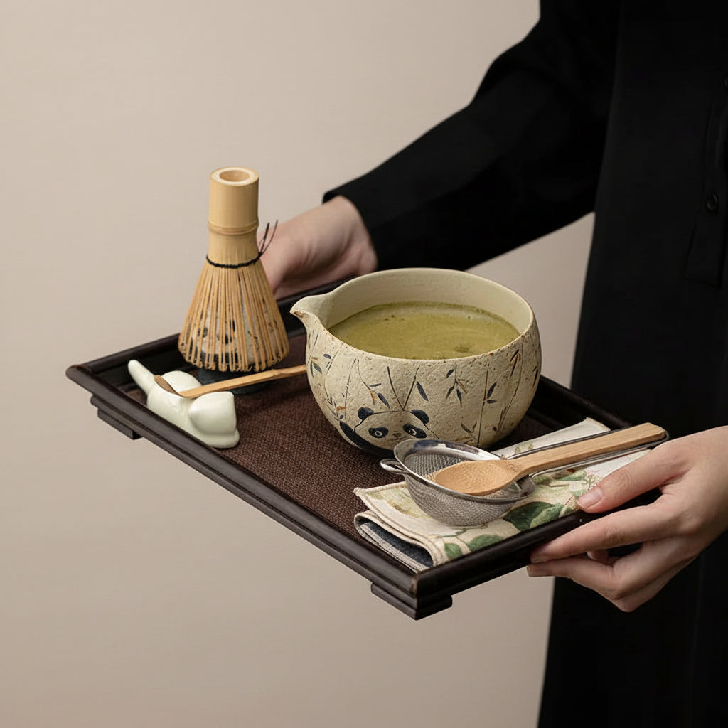 Tea-making set with a teapot, whisk, and other tools on a tray against a black background.